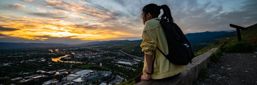 student sitting on M trail looking out over Missoula at sunset