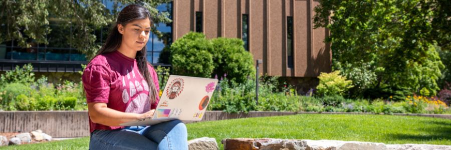 student working on a laptop in the sun outside of the Mansfield Library