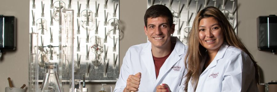 two pharmacy students posing and smiling at the camera with various lab equipment in the background